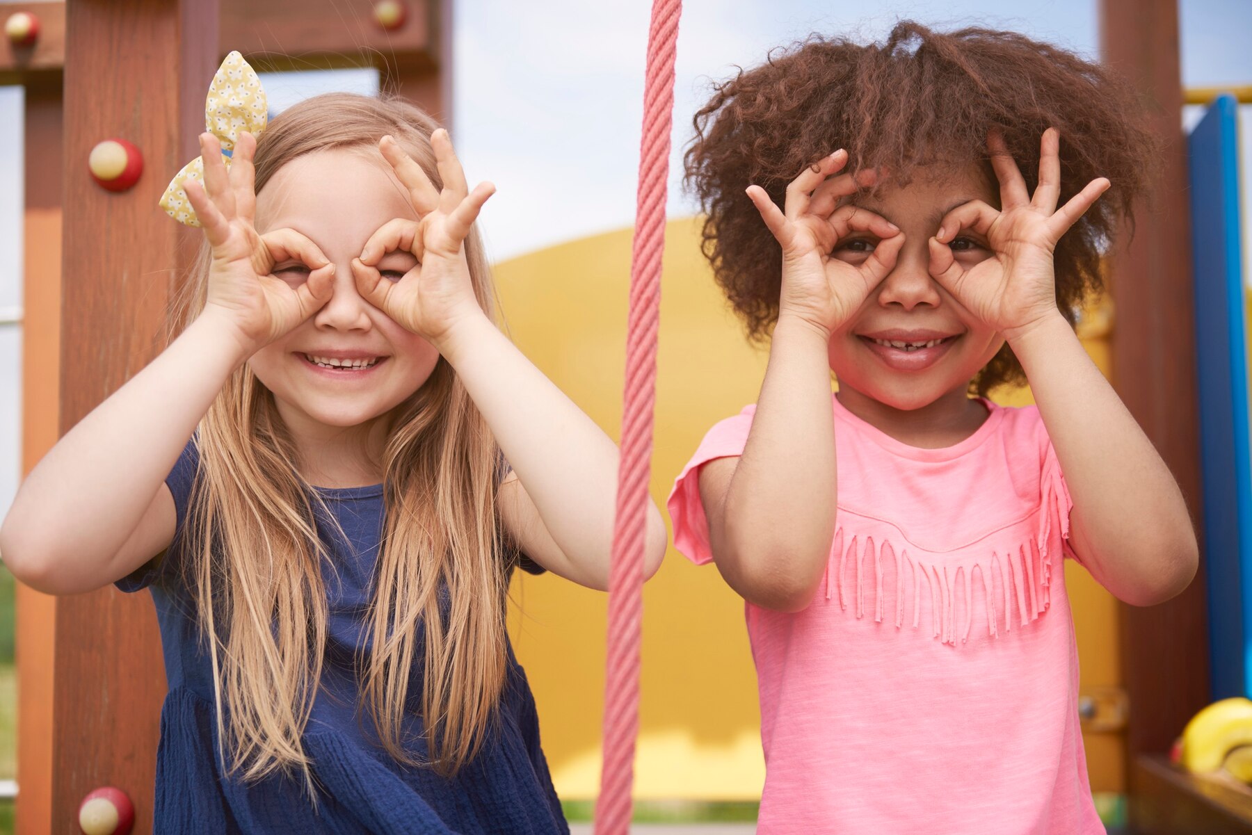 Zwei glückliche Kinder basteln sich aus ihren Fingern Brillen, um durchzusehen